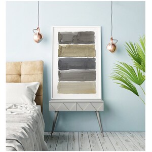 May include: A framed watercolor print featuring five horizontal bands of varying shades of gray and beige. The artwork is displayed on a gray side table with a light blue wall in the background. The room is decorated with modern lighting and a bed.
