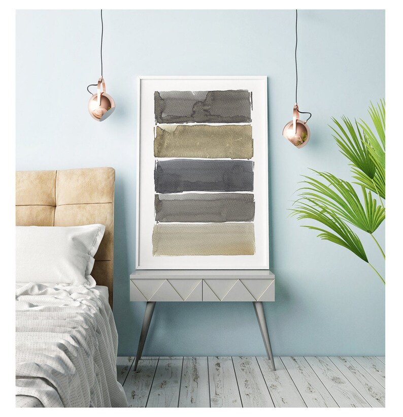 May include: A framed watercolor print featuring five horizontal bands of varying shades of gray and beige. The artwork is displayed on a gray side table with a light blue wall in the background. The room is decorated with modern lighting and a bed.