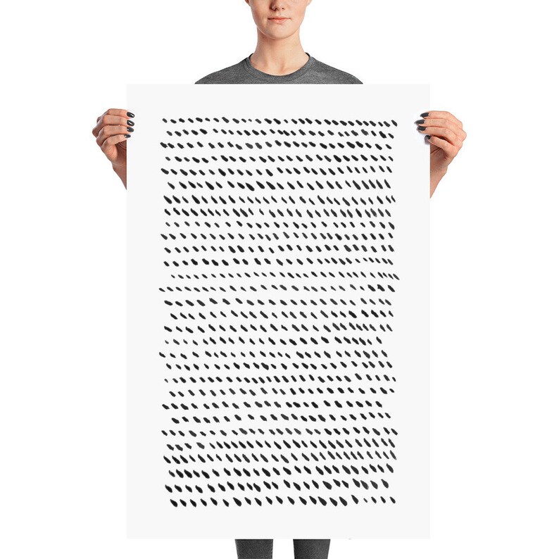 May include: A large, rectangular art print held by a person. The print features a pattern of small, black, diagonal dashes against a white background. The dashes are evenly spaced, creating a textured effect. The artwork is a minimalist, abstract design.