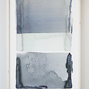 May include: Abstract watercolor painting in a light wood frame. The artwork features three horizontal bands of color: a top and bottom section in shades of blue-gray, and a white band in the middle. The painting has a textured, artistic quality.