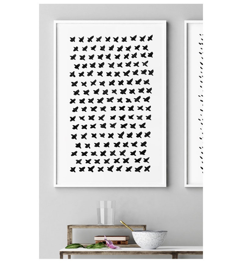 May include: Two framed abstract art prints. The first print features a grid of black brushstroke crosses on a white background. The second print, to the right, has a vertical line of black brushstrokes. Both are in white frames.