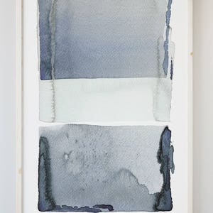 以下が含まれることがあります： 明るい木製フレームに入った抽象的な水彩画。このアートワークは、3 つの水平な色の帯を特徴としています。上部は青灰色、中央は白、下部は青灰色です。絵の端は、テクスチャ加工され、破れたように見えます。