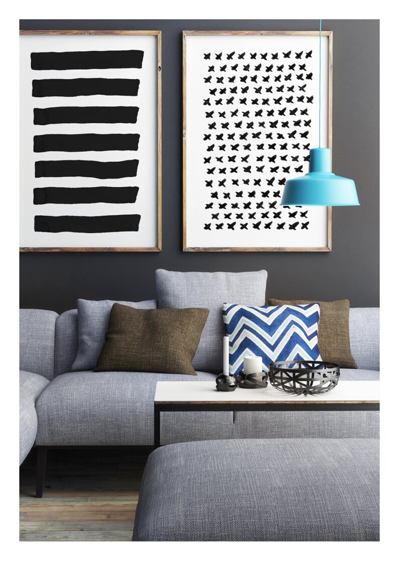 May include: A modern living room scene featuring a gray sofa with brown and blue accent pillows. Two framed abstract art prints hang above the sofa. A light blue pendant lamp hangs from the ceiling. A white coffee table and gray ottoman complete the decor.