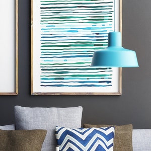 May include: Abstract art print with horizontal lines in shades of blue and green, framed in a light wood. A turquoise pendant lamp hangs above a sofa with throw pillows in gray, brown, and a blue and white chevron pattern. A decorative bowl and candles are on the table.