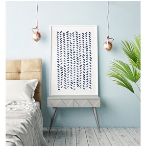 May include: A framed art print featuring a navy blue watercolor pattern of vertical leaf-like shapes on a white background. The artwork is displayed on a gray side table with a light blue wall in the background. The room has a modern, minimalist aesthetic.