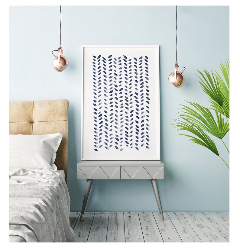 May include: A framed art print featuring a navy blue watercolor pattern of vertical leaf-like shapes on a white background. The artwork is displayed on a gray side table with a light blue wall in the background. The room has a modern, minimalist aesthetic.