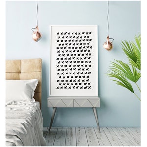 May include: A framed art print featuring a pattern of black butterfly silhouettes on a white background. The artwork is displayed on a gray nightstand with silver legs, set against a light blue wall. The room is decorated with copper-colored pendant lights and a green plant.