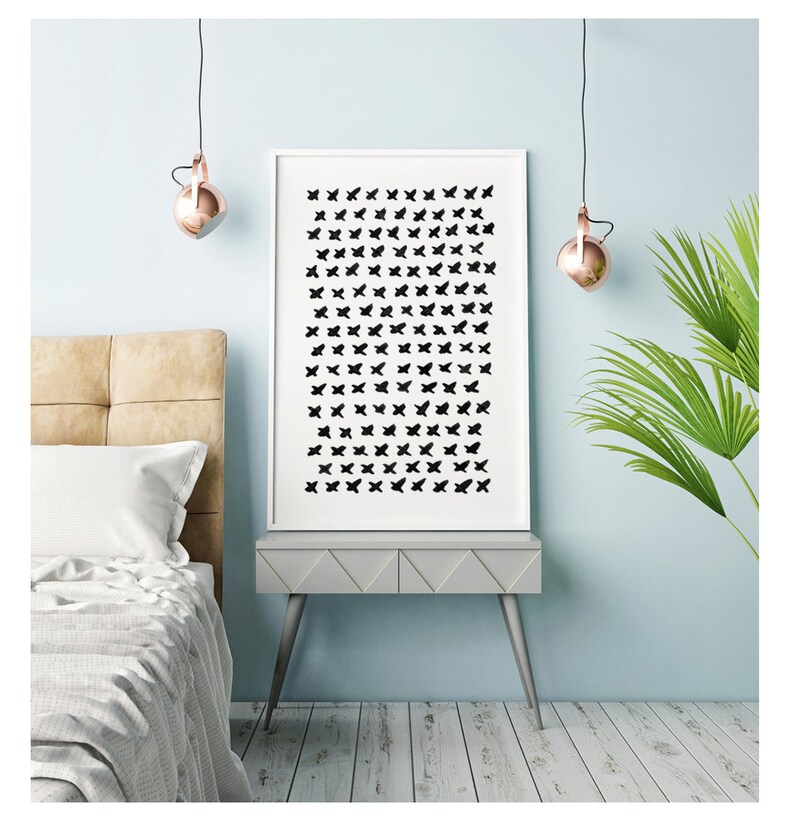 May include: A framed art print featuring a pattern of black butterfly silhouettes on a white background. The artwork is displayed on a gray nightstand with silver legs, set against a light blue wall. The room is decorated with copper-colored pendant lights and a green plant.