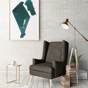 May include: A modern living room scene featuring a dark gray wingback chair with light wood legs. A framed abstract teal painting hangs on a white brick wall. A side table with a teapot and a gold lamp complete the decor.