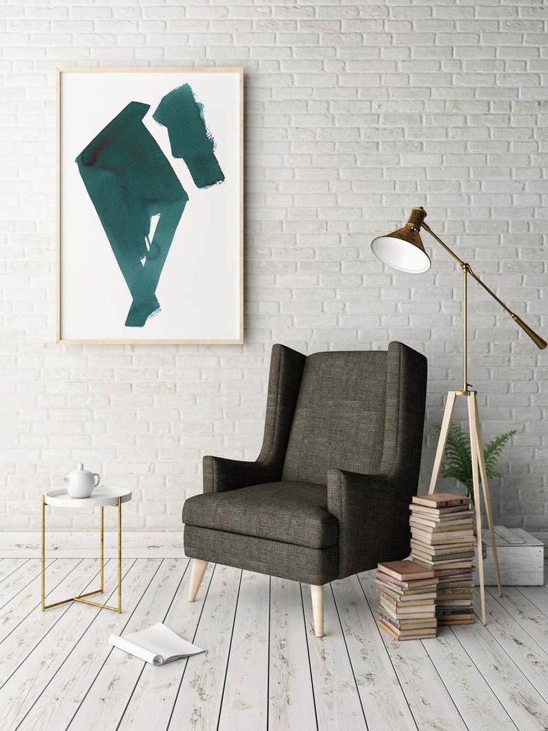 May include: A modern living room scene featuring a dark gray wingback chair with light wood legs. A framed abstract teal painting hangs on a white brick wall. A side table with a teapot and a gold lamp complete the decor.