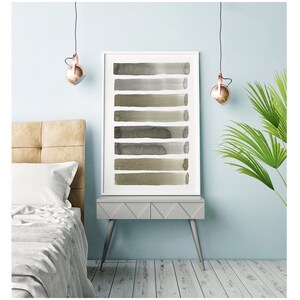 May include: A framed art print featuring a series of horizontal watercolor brushstrokes in shades of gray and olive green. The artwork is displayed on a gray side table with a light blue wall backdrop. The room is decorated with a bed and a hanging light fixture.