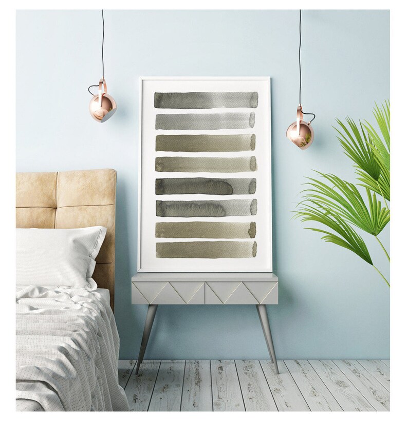 May include: A framed art print featuring a series of horizontal watercolor brushstrokes in shades of gray and olive green. The artwork is displayed on a gray side table with a light blue wall backdrop. The room is decorated with a bed and a hanging light fixture.
