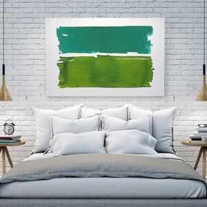 Op de afbeelding: Abstract kunstwerk met twee horizontale aquarelblokken in groentinten. Het bovenste blok is blauwgroen, de onderste is een lichter groen. Het kunstwerk hangt boven een bed met wit beddengoed, met houten nachtkastjes aan weerszijden.