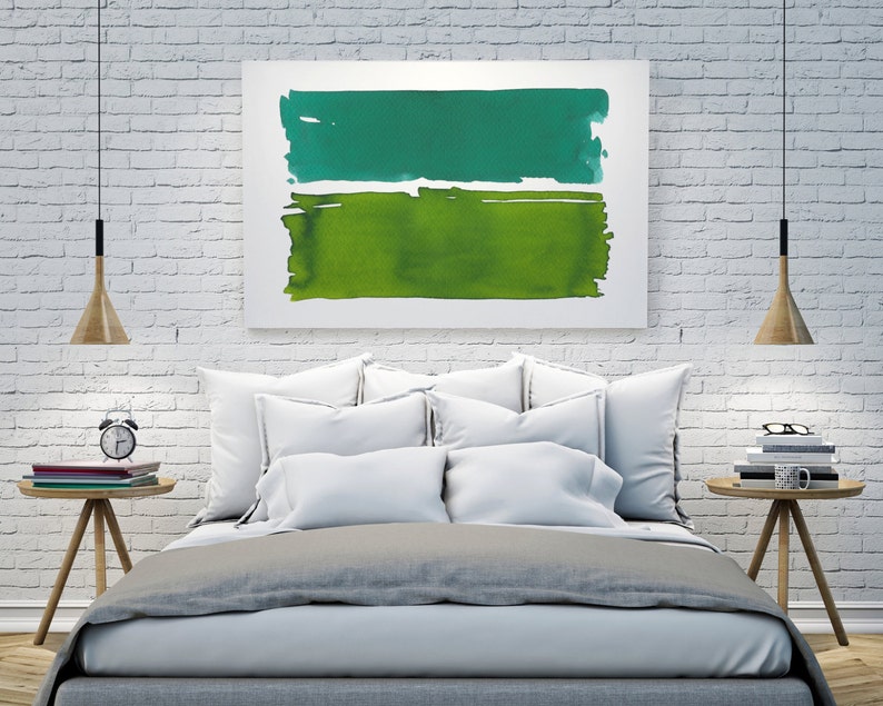 Op de afbeelding: Abstract kunstwerk met twee horizontale aquarelblokken in groentinten. Het bovenste blok is blauwgroen, de onderste is een lichter groen. Het kunstwerk hangt boven een bed met wit beddengoed, met houten nachtkastjes aan weerszijden.