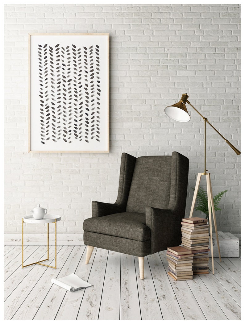May include: A framed abstract art print with a neutral color palette hangs above a wingback chair. The print features a pattern of black and gray leaf-like shapes. A small side table with a white top and gold legs sits nearby.