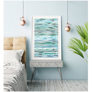 May include: A framed abstract art print featuring horizontal lines in shades of blue and green. The artwork is displayed on a gray nightstand next to a bed with a beige headboard. The room has a light blue wall and copper-colored pendant lights.