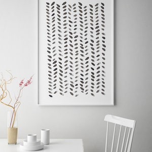 May include: A framed abstract art print featuring a pattern of dark gray leaf-like shapes arranged in vertical rows against a white background. The artwork is displayed on a white wall above a white table and chair.
