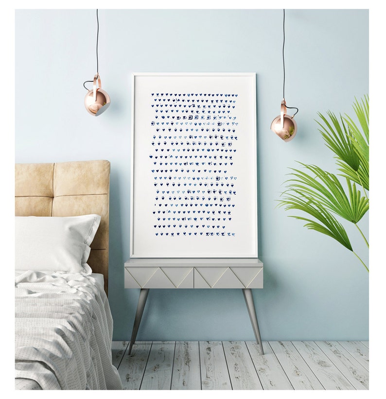 May include: A framed art print featuring a pattern of blue hearts and abstract shapes on a white background. The artwork is displayed on a gray side table with a light blue wall backdrop. The room has a modern aesthetic with copper-colored pendant lights.
