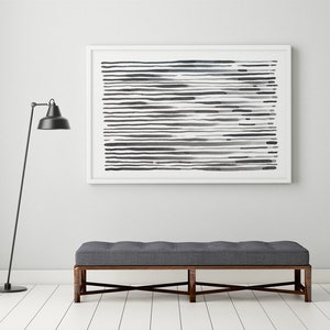May include: A modern interior scene featuring a framed abstract artwork with horizontal black and gray lines. Below, a gray upholstered bench with a dark wooden frame sits on a white floor. A black floor lamp stands to the left, adding to the contemporary aesthetic.