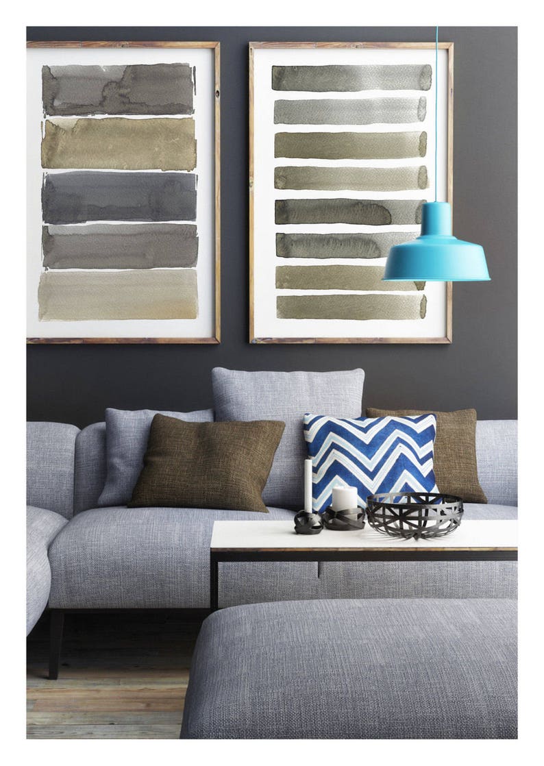 May include: Two framed watercolor paintings with horizontal brushstrokes in neutral tones hang above a gray sofa with brown and blue accent pillows. A turquoise pendant lamp hangs from the ceiling, adding a pop of color.