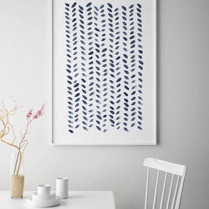 May include: A framed art print featuring a watercolor design of navy blue leaf-like shapes arranged in vertical rows. The artwork is displayed on a white wall above a white table with minimalist decor, including a vase and white dishes.