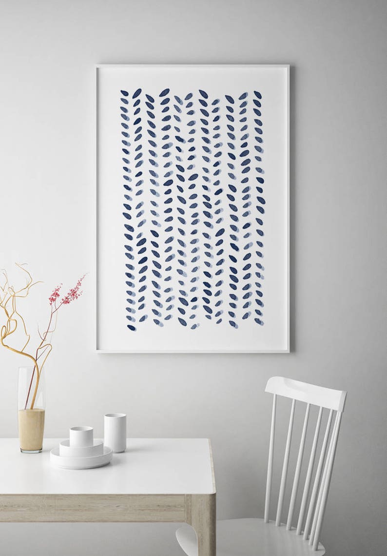 May include: A framed art print featuring a watercolor design of navy blue leaf-like shapes arranged in vertical rows. The artwork is displayed on a white wall above a white table with minimalist decor, including a vase and white dishes.