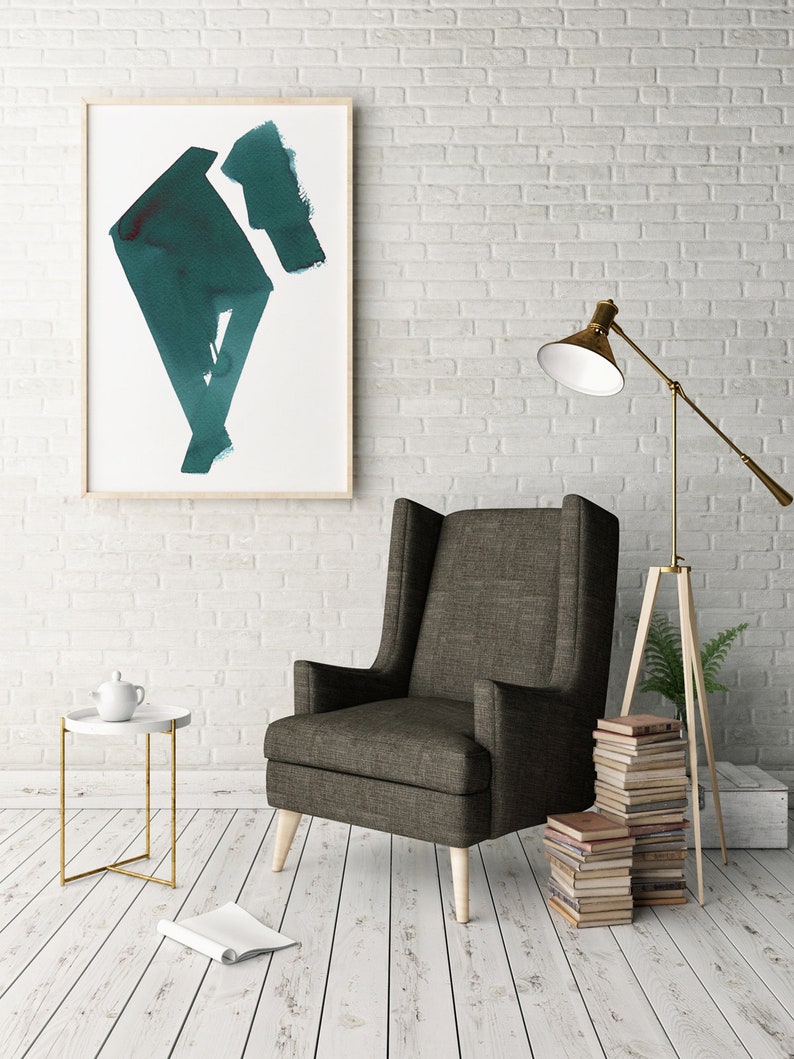 May include: An interior design scene featuring a tall, dark gray armchair with light wooden legs. A framed abstract teal painting hangs on a white brick wall. A side table with a teapot and a floor lamp are also visible.