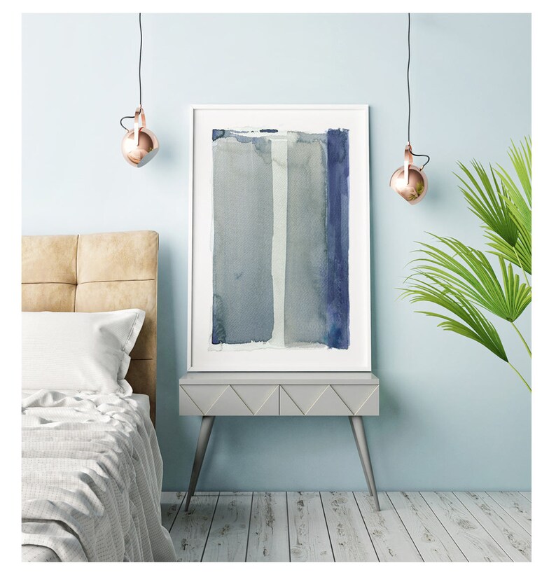 May include: A framed abstract watercolor painting with vertical stripes in shades of blue and gray. The artwork is displayed on a gray nightstand with silver legs, next to a bed with a beige headboard. Copper-colored pendant lights hang above.