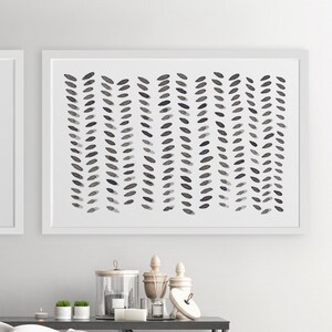 May include: Abstract art print in a white frame. The artwork features a pattern of vertical rows of dark gray, leaf-like shapes on a white background. The print is displayed above a table with decorative items.