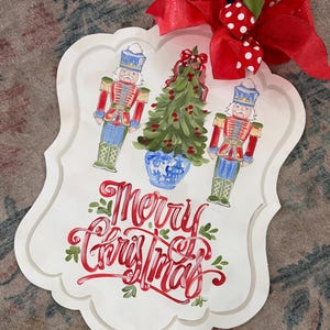 May include: White wooden sign with a red and green Christmas tree, two toy soldiers, and the words "Merry Christmas" in red cursive.