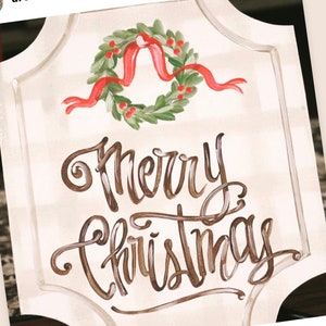 May include: A decorative sign with a watercolor design. The sign features the words "Merry Christmas" in brown script, with a wreath of green leaves, red berries, and a red ribbon at the top. The background has a subtle plaid pattern.