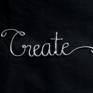 May include: A silver wire sculpture of the word "Create" on a black background.