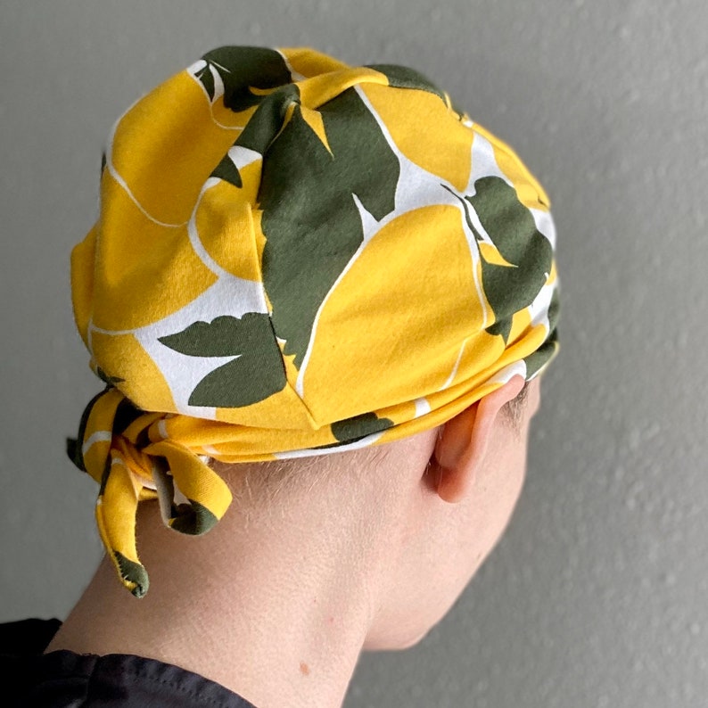 May include: A yellow and green patterned fabric hat with a tie. The hat has a floral design with white accents.