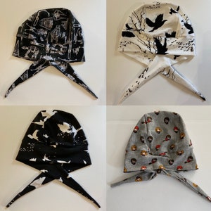 May include: Four different fabric head coverings with ties. The head coverings are black and white with various patterns, including birds, stars, and a graphic print. The head coverings are tied at the back of the neck.