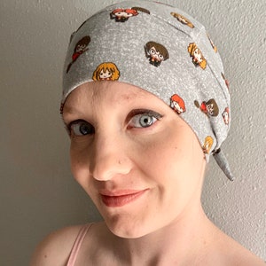 May include: A gray and white patterned fabric head covering with a tie at the back. The pattern features small images of characters from the Harry Potter series.