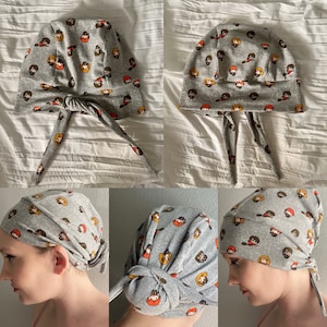 May include: A gray fabric headband with a pattern of cartoon characters. The headband is tied in a knot at the top and has long ties that hang down the back.