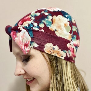May include: A burgundy floral print turban headband with a knotted bow on the side. The headband is made of a soft, stretchy fabric.