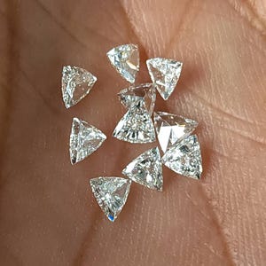 close up of several trillion cut natural diamonds in palm, calibrated 3x3mm triangle stones arranged to show consistent shape and size, ideal for matched pairs and layouts, natural daylight sparkle F G VVS VS