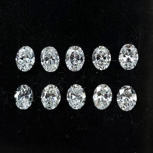 May include: Ten oval-cut diamonds displayed on a black surface. The clear diamonds sparkle, reflecting light. The stones are of similar size and shape, suggesting a matched set for jewellery making or design.