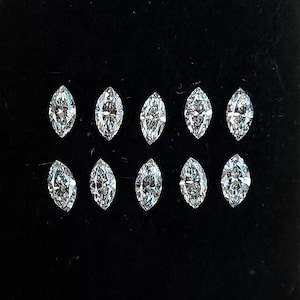 Pode incluir: Uma caixa de plástico transparente contendo onze diamantes de corte marquesa. Os diamantes estão dispostos em duas fileiras sobre um fundo preto. Os diamantes são pequenos e brilhantes.