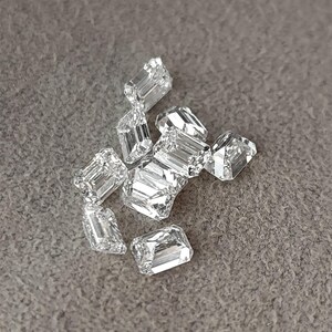 Angled close up of an emerald cut diamond on grey fabric, with step facets catching the light and giving strong reflections.