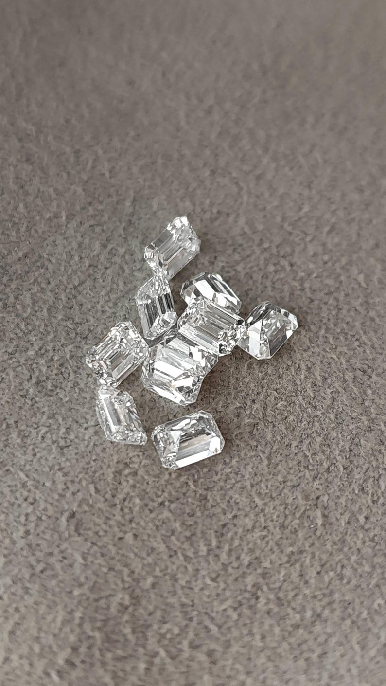 Angled close up of an emerald cut diamond on grey fabric, with step facets catching the light and giving strong reflections.