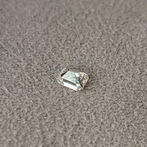 Single emerald cut diamond lying on a wooden surface, clearly showing the rectangular outline and faceting of the 3x2mm or 4x3mm calibrated stone.