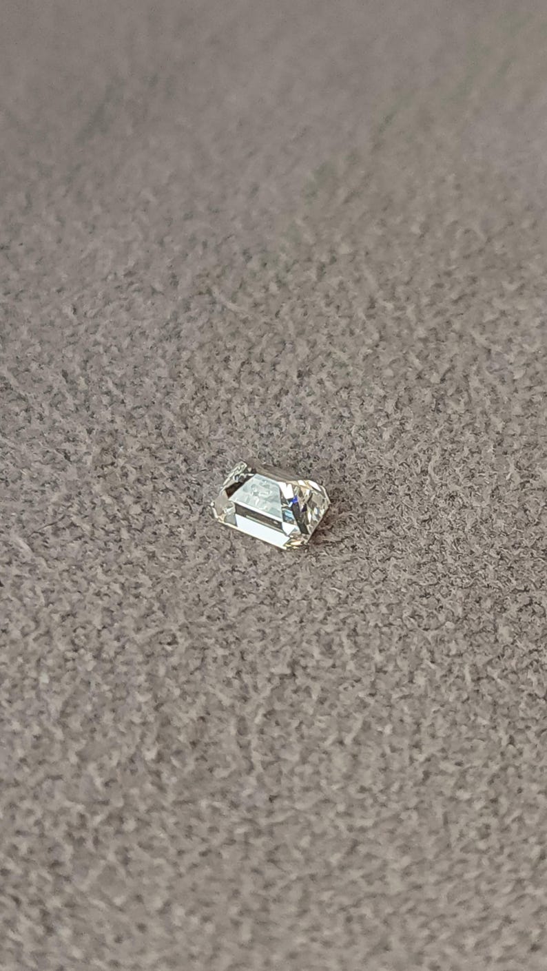 Single emerald cut diamond lying on a wooden surface, clearly showing the rectangular outline and faceting of the 3x2mm or 4x3mm calibrated stone.