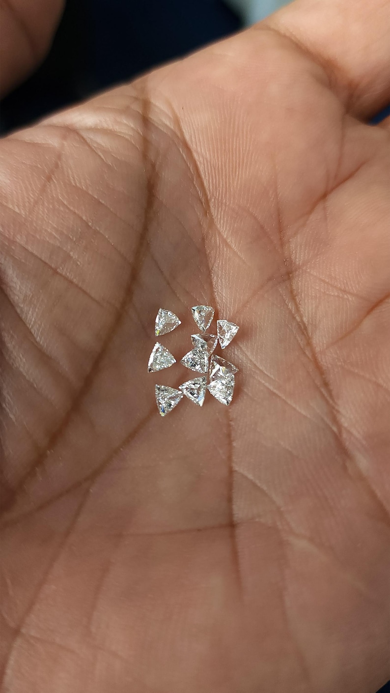 group of calibrated trillion cut natural diamonds shown in hand, multiple 3x3mm triangle side stones displayed for matching sets, jewelry supply for rings earrings and pendants, F G near colorless VVS VS