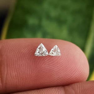single 3x3mm trillion cut natural diamond on fingertip macro view, triangle side stone for engagement ring accents, clean face up sparkle in natural daylight, F G color VVS VS clarity, calibrated loose diamond