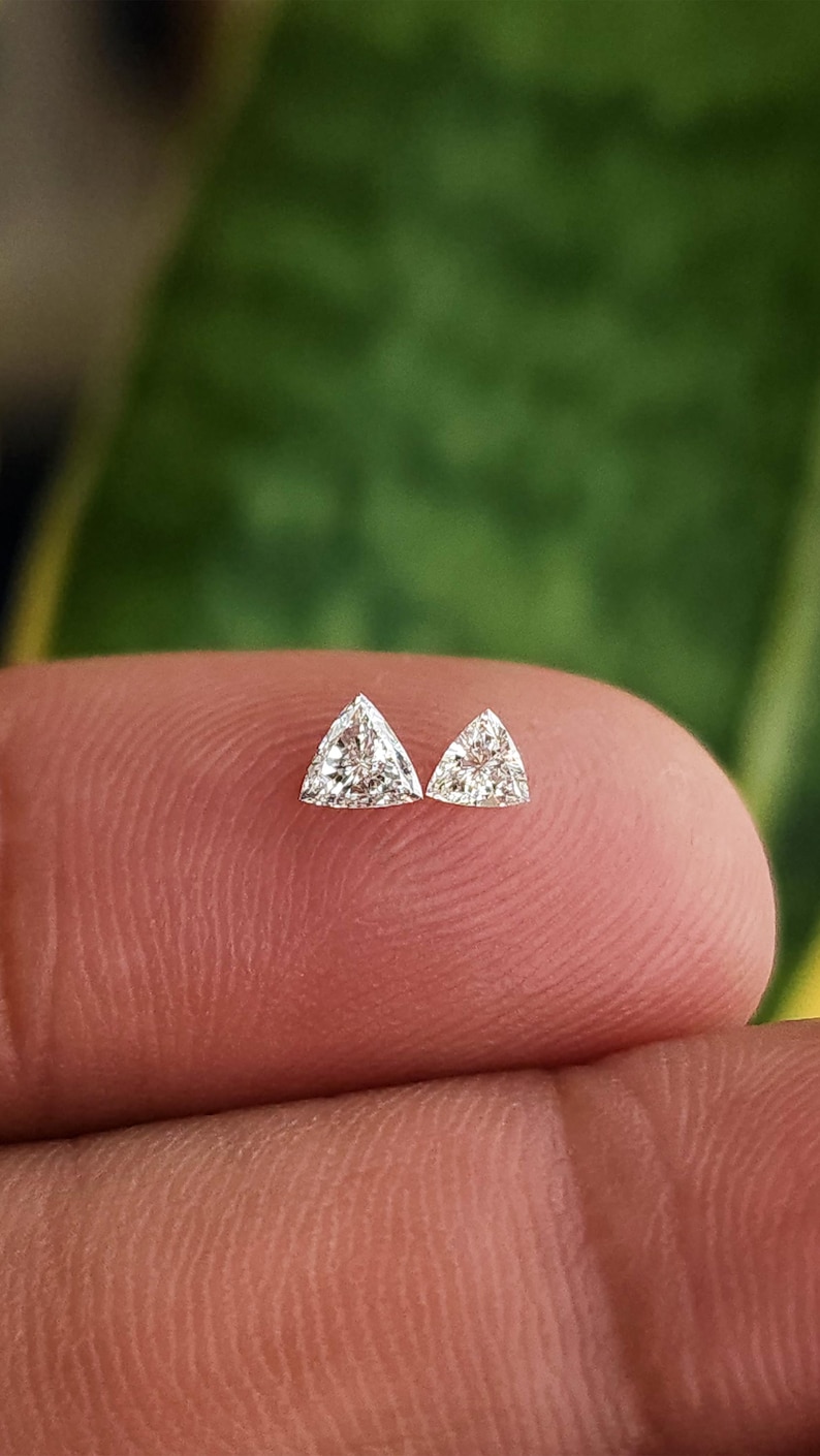 single 3x3mm trillion cut natural diamond on fingertip macro view, triangle side stone for engagement ring accents, clean face up sparkle in natural daylight, F G color VVS VS clarity, calibrated loose diamond