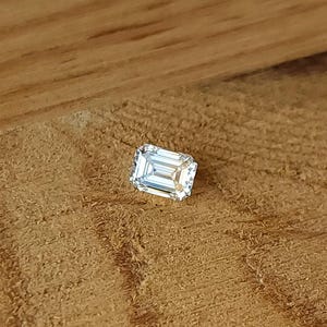 Side view of an emerald cut diamond in tweezers outdoors, focusing on girdle thickness and pavilion depth for secure setting.