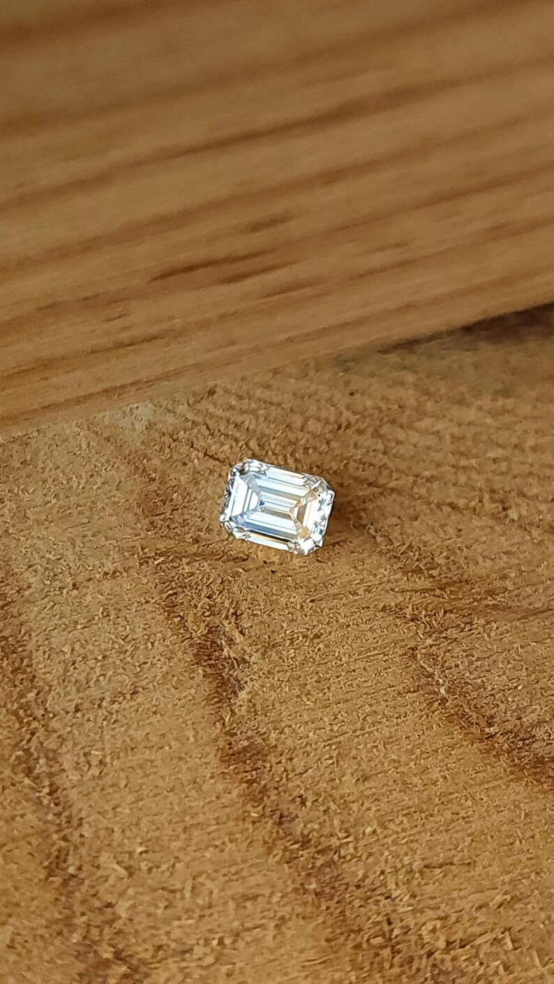 Side view of an emerald cut diamond in tweezers outdoors, focusing on girdle thickness and pavilion depth for secure setting.