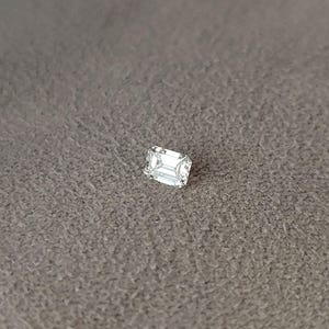 Side view of an emerald cut diamond in tweezers outdoors, focusing on girdle thickness and pavilion depth for secure setting.